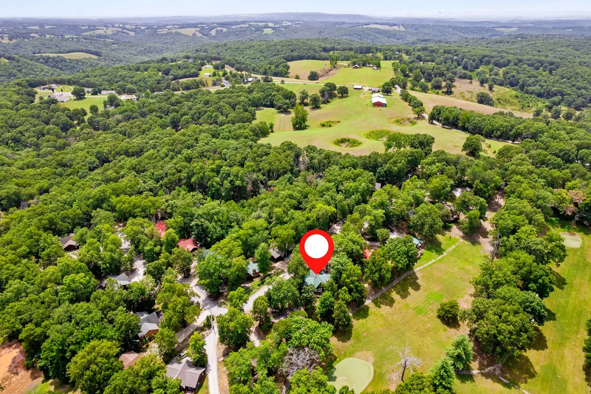 A tranquil exterior view of the resort grounds showing dense tree cover, open fields, and scattered residential structures. The scene evokes a sense of openness and natural beauty, ideal for guests and their pets to enjoy walks and exploration.