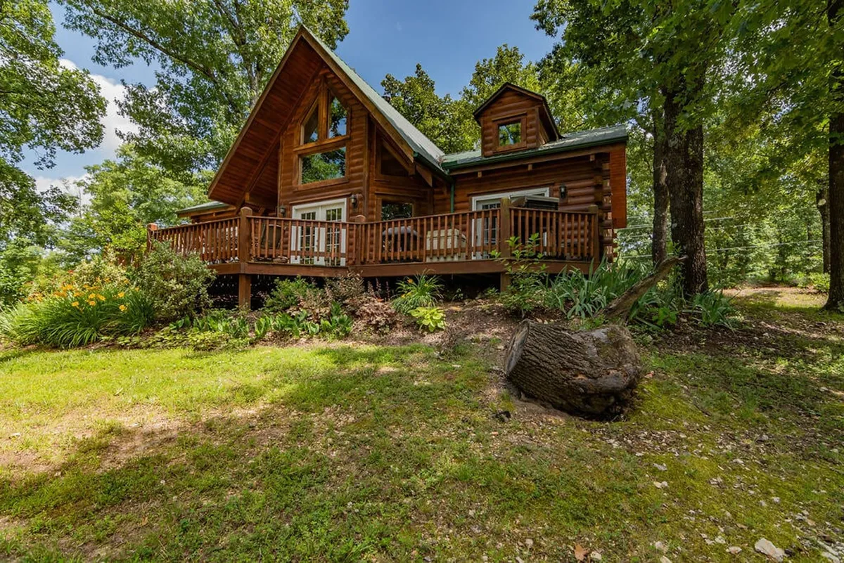 A wide-angle view of the cabin’s spacious deck, surrounded by lush greenery. The deck offers ample space for outdoor dining or relaxing, with the natural setting emphasizing peace and privacy after the excitement of local events.