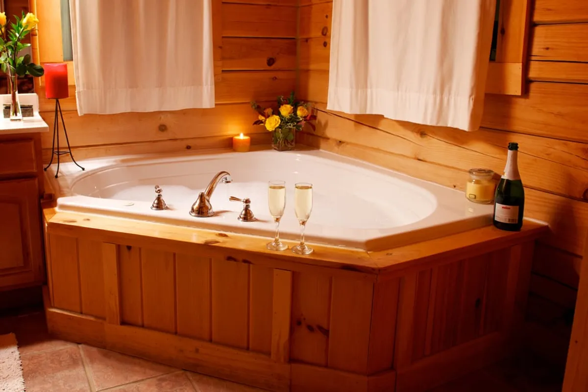 This interior shot centers on a luxurious jacuzzi tub surrounded by candles, champagne glasses, and fresh flowers. The ambiance is romantic and relaxing, with warm lighting creating an intimate atmosphere.