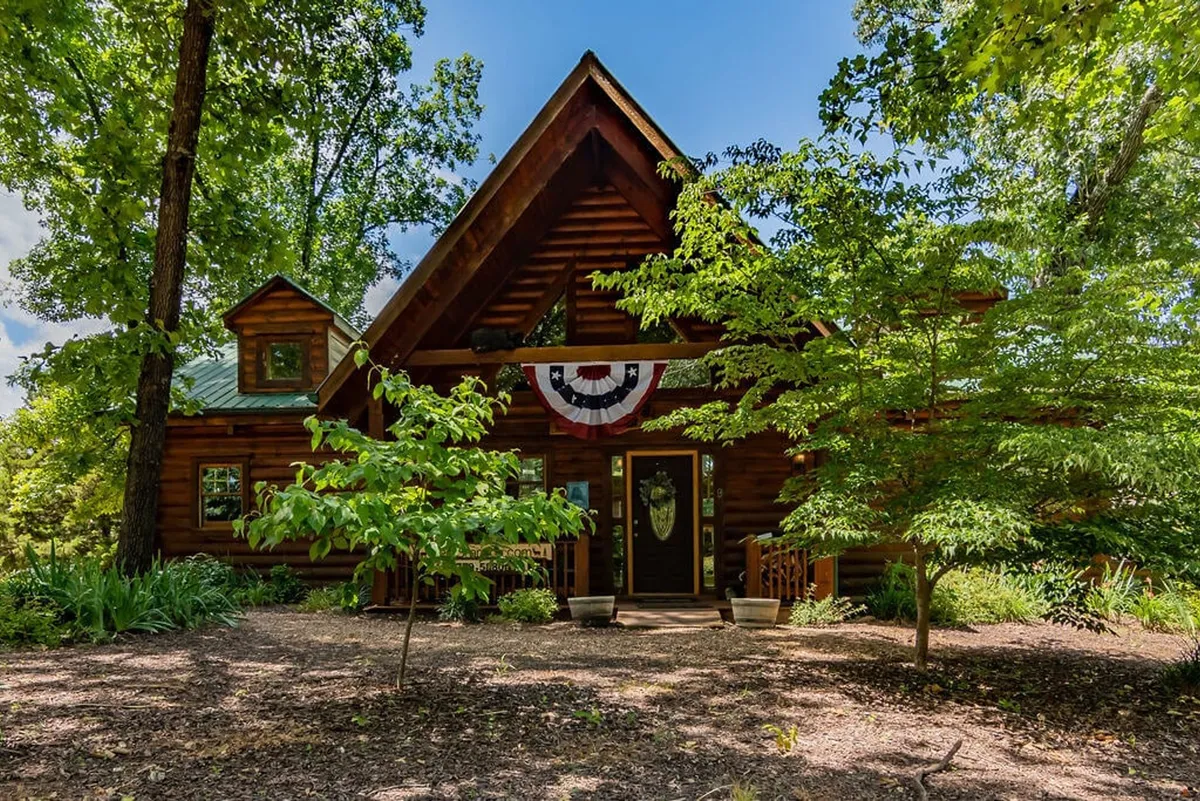 This image showcases the front exterior of a charming log cabin, complete with a welcoming front porch adorned with potted plants and festive decorative bunting. The inviting porch hints at a peaceful retreat after busy event-filled nights.