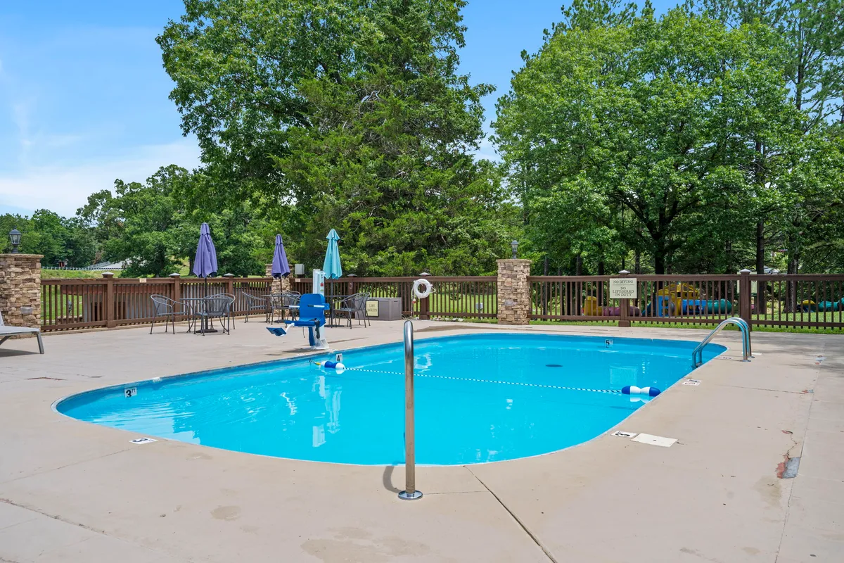 A lively resort pool area is surrounded by mature trees and offers plenty of lounge chairs and umbrellas for group relaxation. The setting invites guests to enjoy swimming, sunbathing, and socializing in a communal environment, emphasizing leisure and shared experiences.