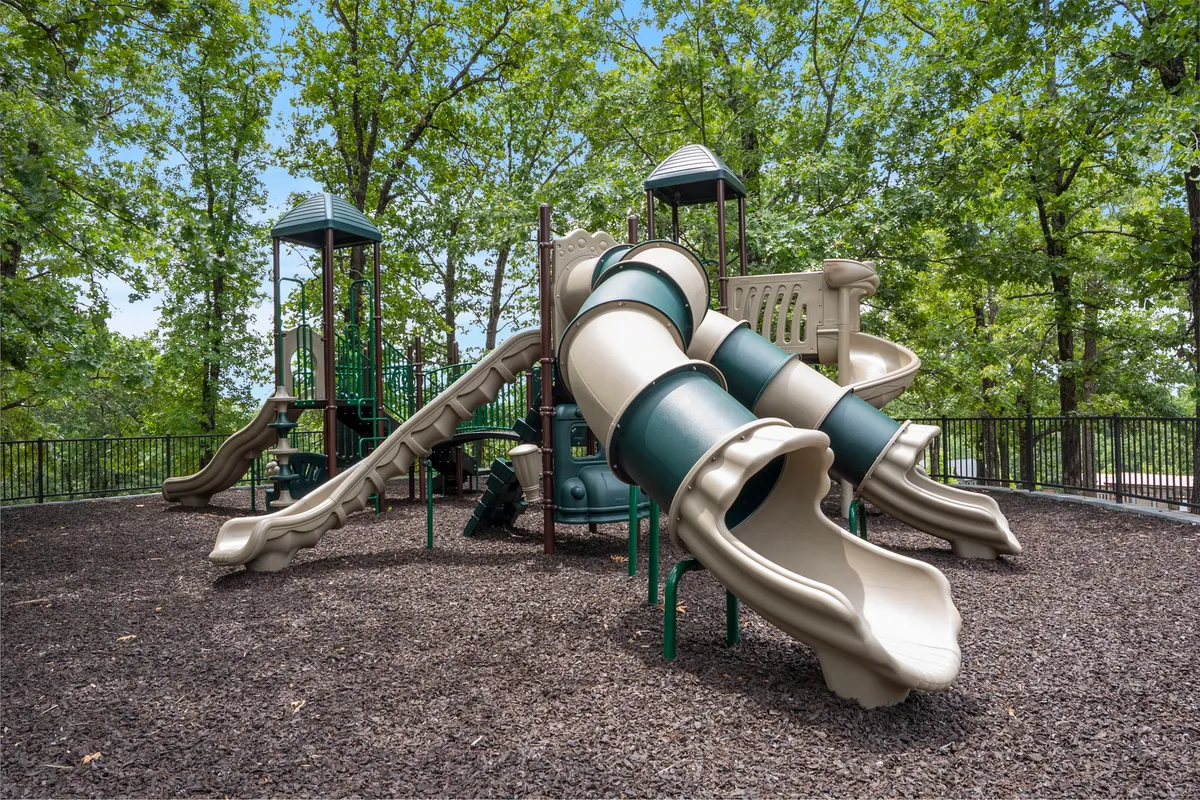 A bright, joyful outdoor playground surrounded by trees, featuring slides and climbing structures. The space is designed for energetic play and family gatherings, with plenty of green surroundings.