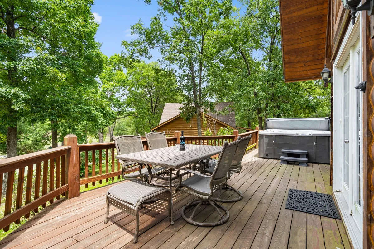 This exterior image features a spacious deck with an outdoor dining table and a private hot tub surrounded by towering trees, providing a tranquil woodland backdrop. The layout encourages outdoor dining and group relaxation, making it ideal for socializing or unwinding together.