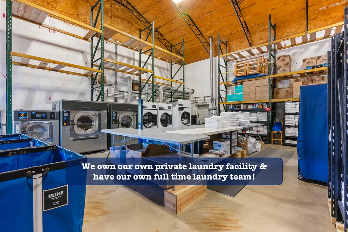 A professional-grade laundry facility with industrial washers and dryers, a folding table, and shelves stocked with clean linens and supplies. The space is organized and exudes cleanliness and efficiency.